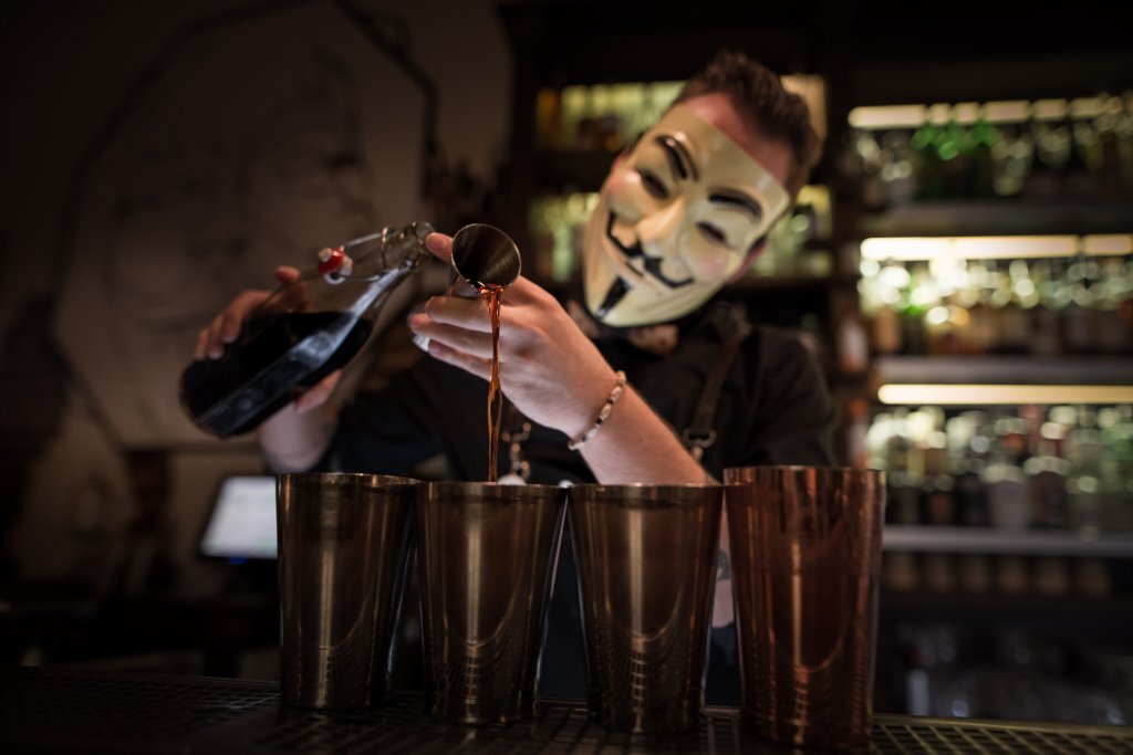 Masked bartender pouring a cocktail at AnonymouS Bar in Prague