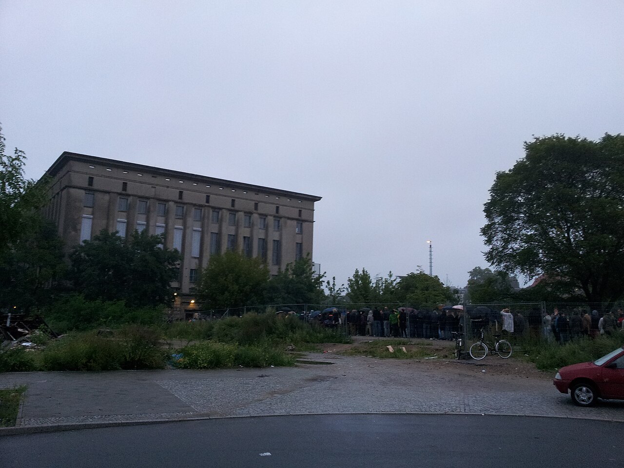 The queue outside Berghain nightclub in Berlin at dusk, people lined up along the fence.