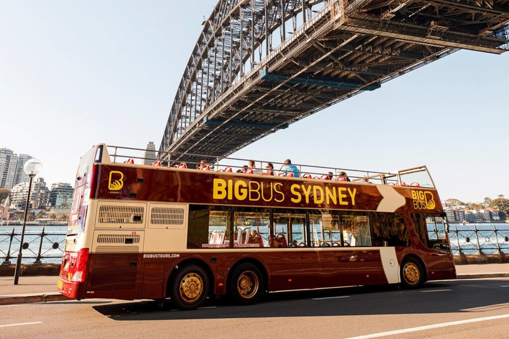 Red open-top sightseeing bus passing landmarks in Sydney